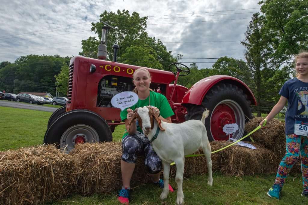 woman with goat in front of tractor holding a sign "I ran with the goats"